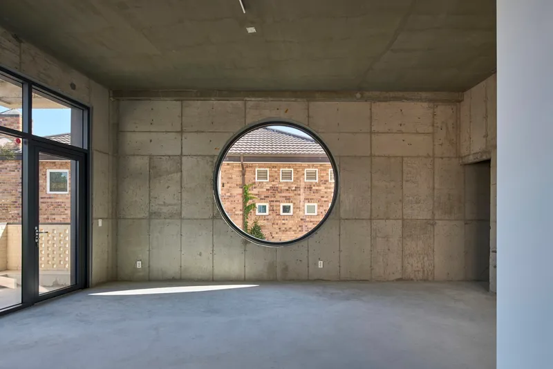 Interior room with board-formed concrete walls and a large circular window framing neighboring buildings