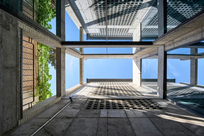 Upward view through an open courtyard framed by concrete floors and perforated metal screens above