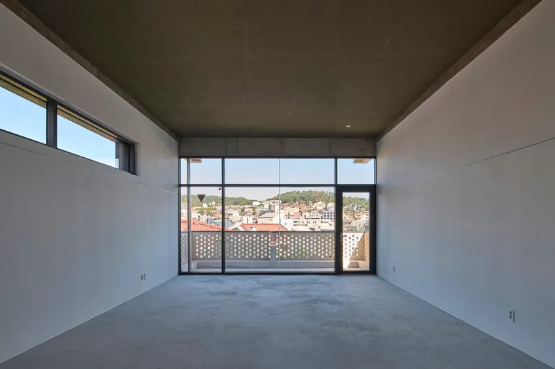 Empty interior room with concrete ceiling and glazed wall opening to perforated screen and rooftops beyond
