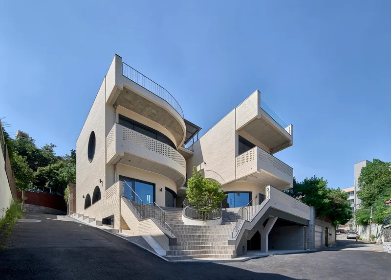 Street view of the stacked volumes with curved balconies and perforated brick screens under a clear sky