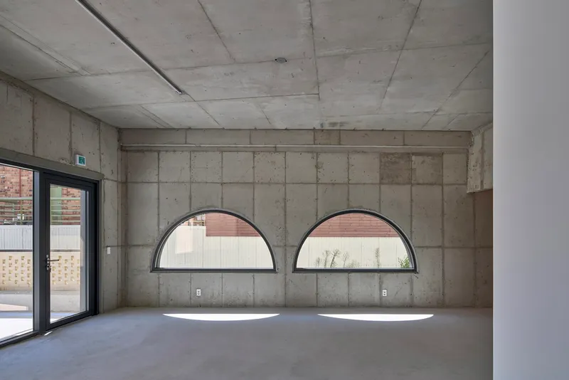 Exposed concrete interior wall with two semicircular windows casting shadows on the polished floor