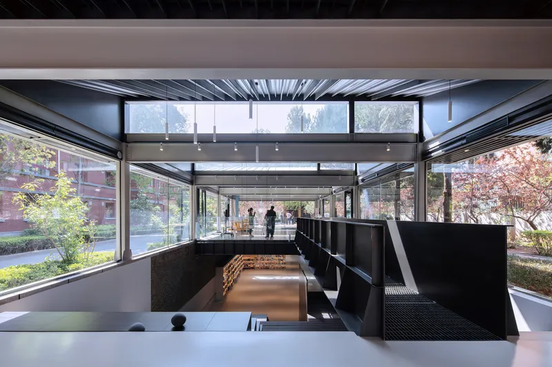 Split-level space with black shelving and perforated metal stairs framed by floor-to-ceiling glass overlooking courtyard gardens