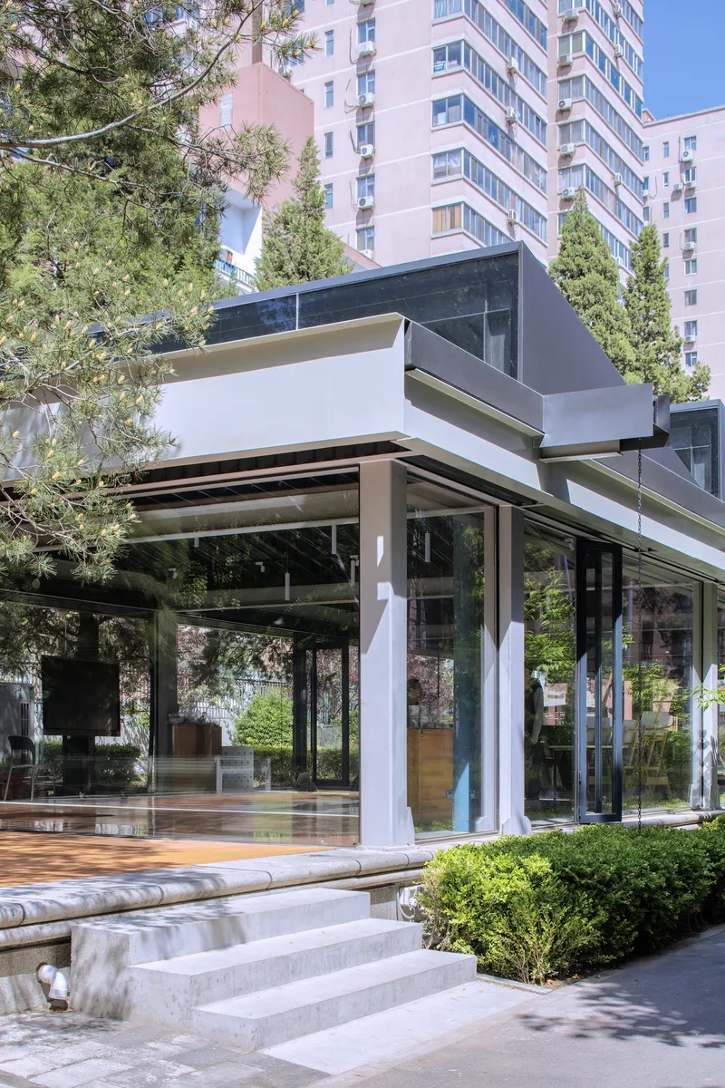 Glass pavilion with white columns and folded roof planes set against a residential tower