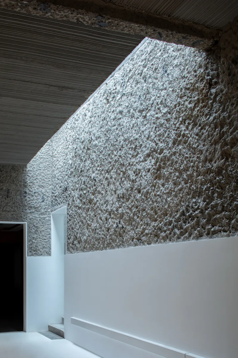 Interior view of a textured stone wall illuminated by natural light through a ribbed ceiling