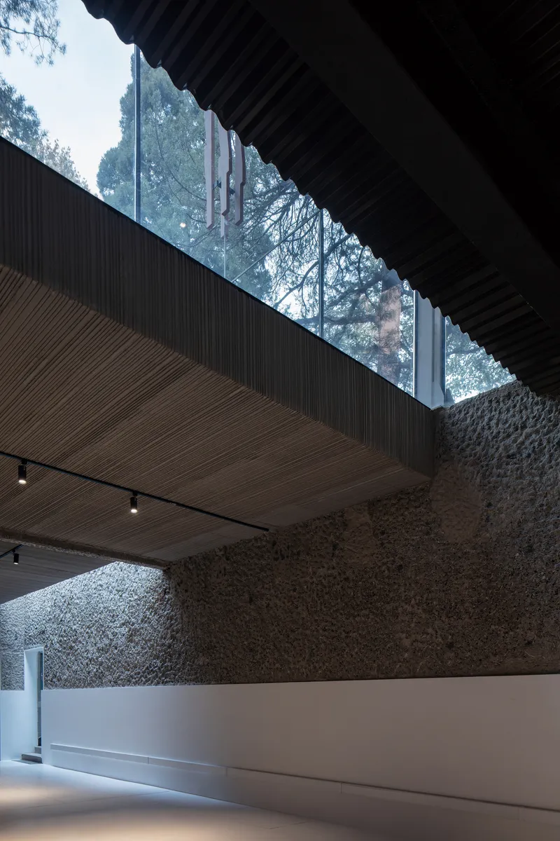 Double-height interior space with rough stone walls and a linear skylight between corrugated ceiling planes
