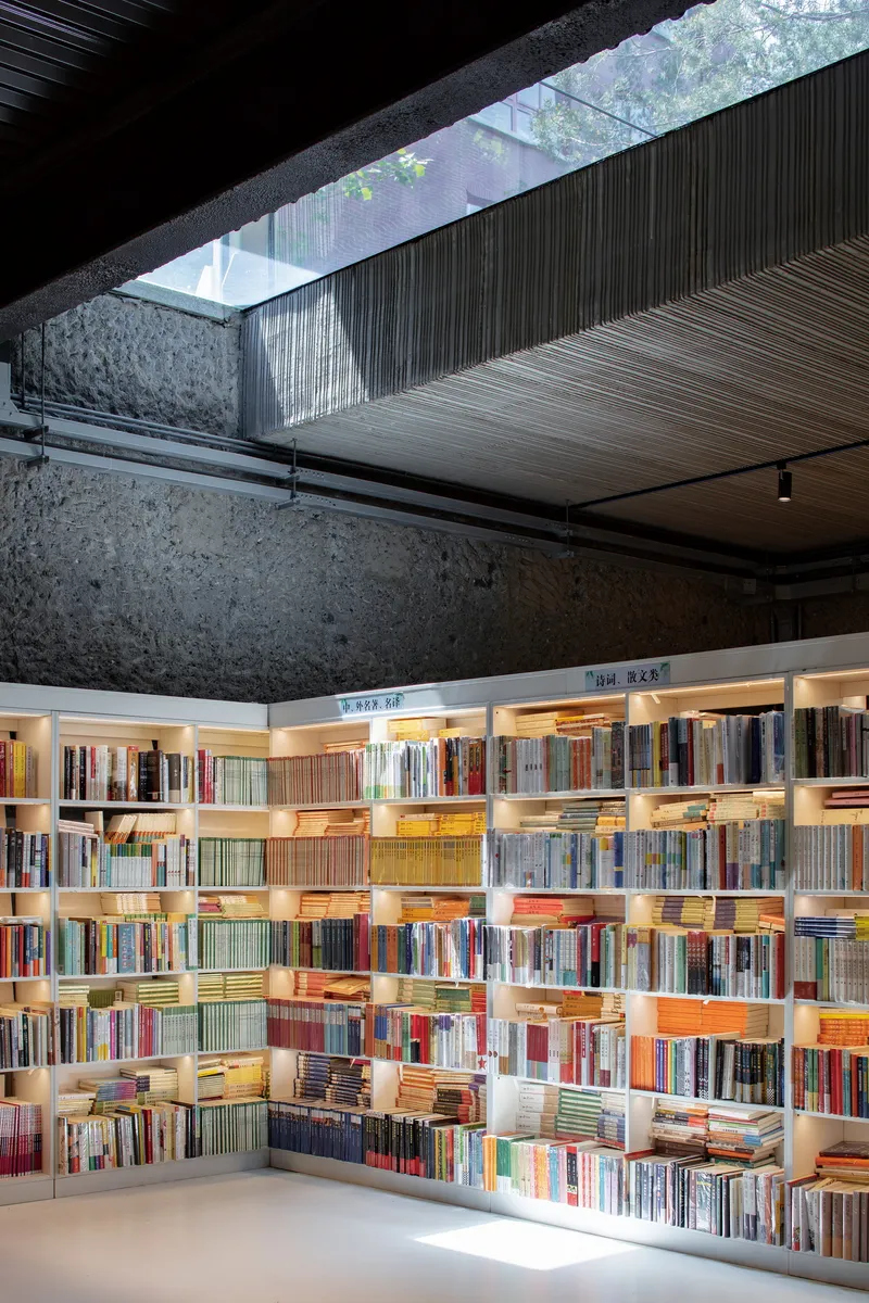 Corner view showing illuminated book display beneath a linear skylight and aggregate concrete walls