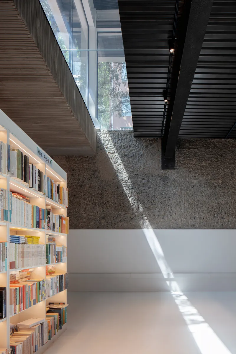 Sunlight cutting across polished floor from clerestory glazing above bookshelf and textured stone wall
