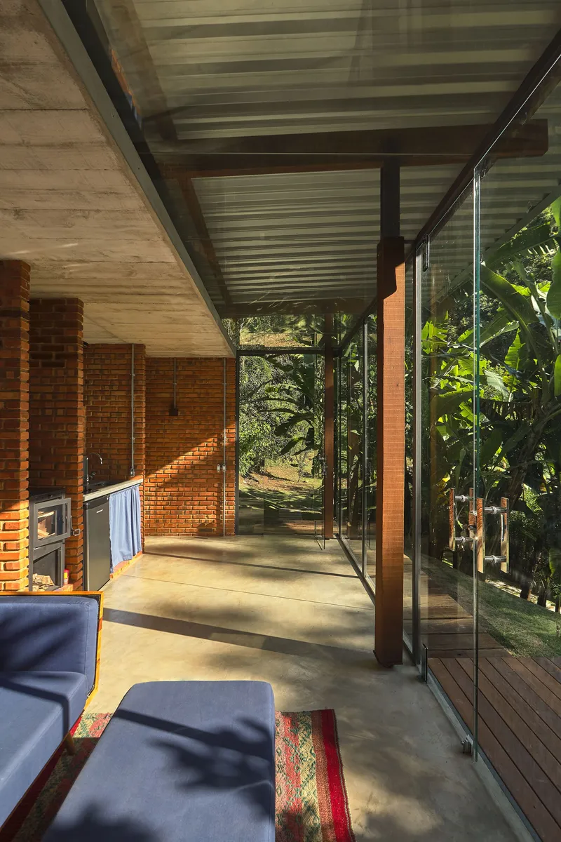 Interior view showing exposed brick wall with fireplace and glass walls opening to the forest beyond