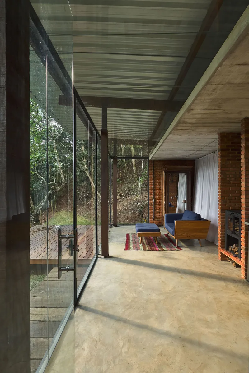 Living space with floor-to-ceiling glass walls revealing timber deck and hillside vegetation under an overcast sky