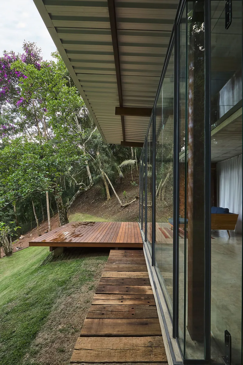 Timber stairs descending alongside a glazed facade with deck and lawn on a wooded slope
