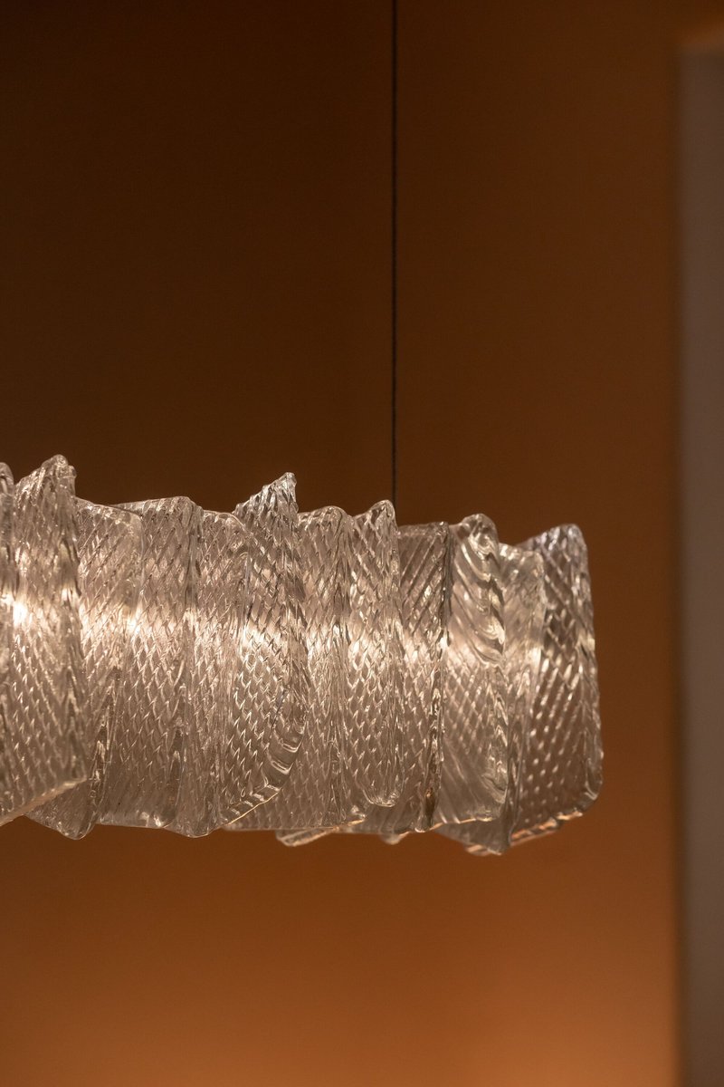 Textured glass pendant light with rippled surfaces suspended against a wood paneled wall