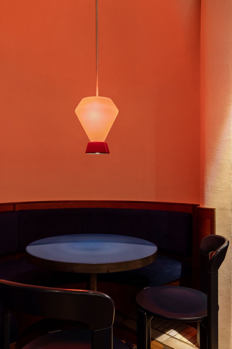 Banquette seating with round table beneath a frosted glass pendant in a coral-painted alcove