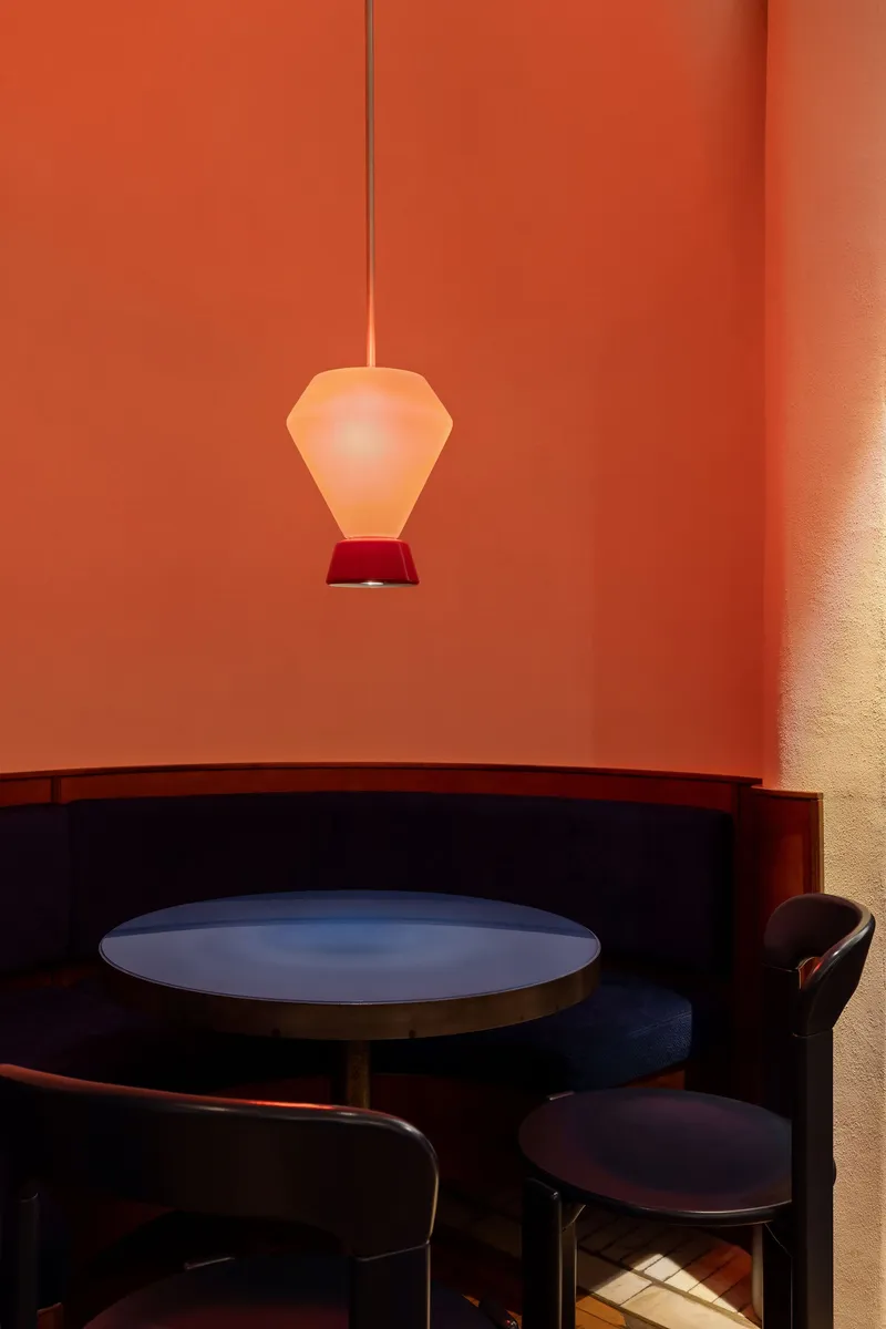 Banquette seating with round table beneath a frosted glass pendant in a coral-painted alcove