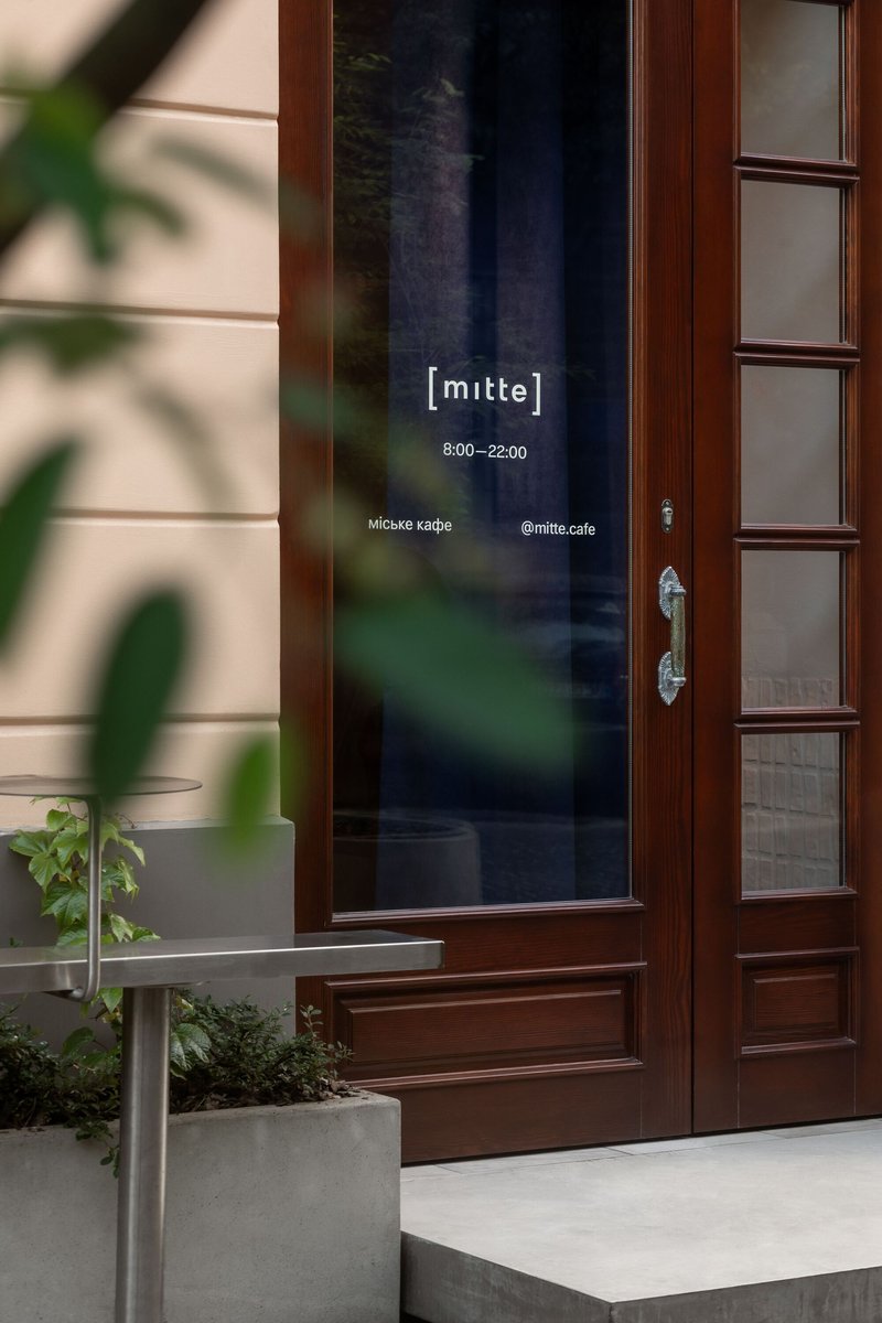 Timber framed entrance door with glazed panel, flanked by potted plants in afternoon light