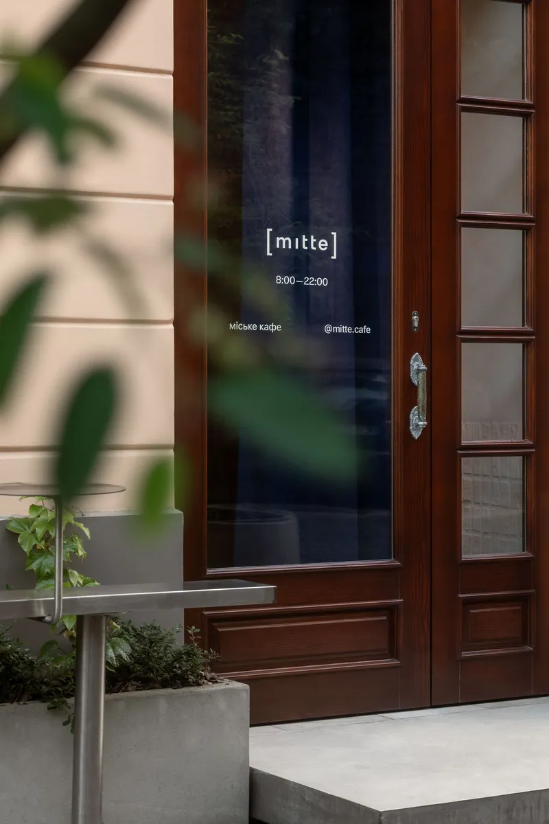 Timber framed entrance door with glazed panel, flanked by potted plants in afternoon light