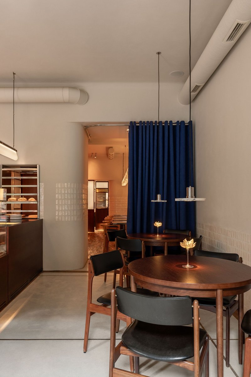 Interior cafe space with exposed ductwork, blue fabric divider, and timber furniture under pendant lighting