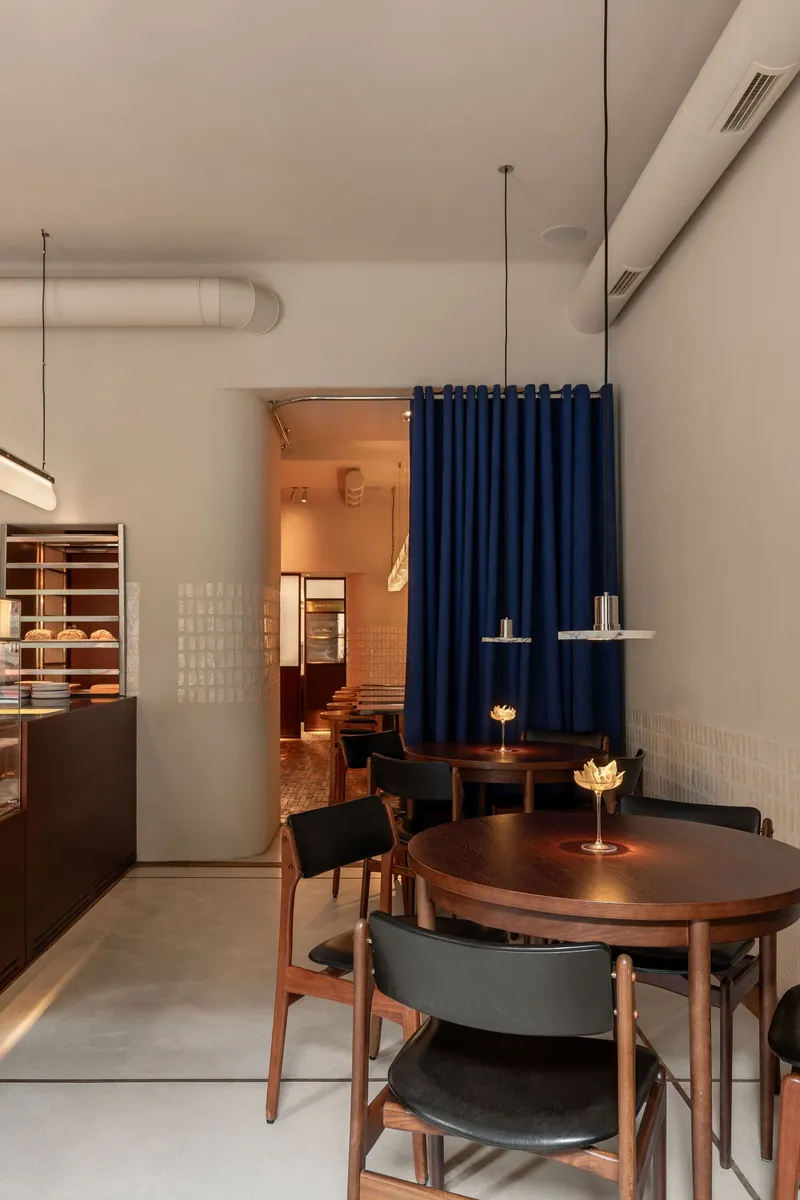 Interior cafe space with exposed ductwork, blue fabric divider, and timber furniture under pendant lighting