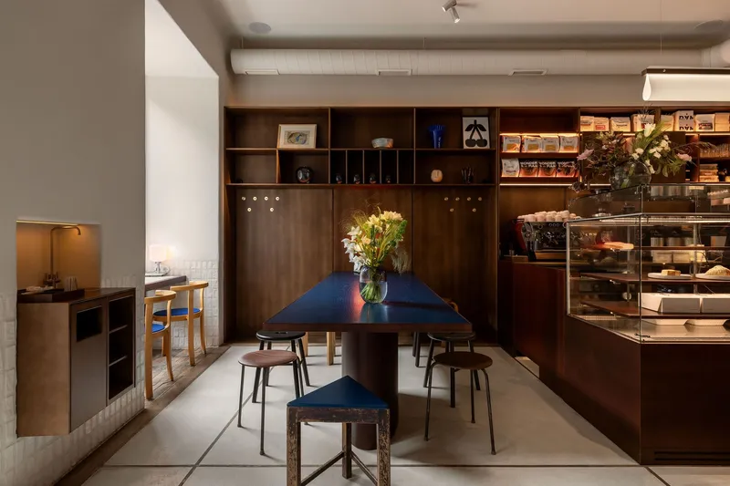 Central dining table with timber shelving wall and glass display cases in afternoon light