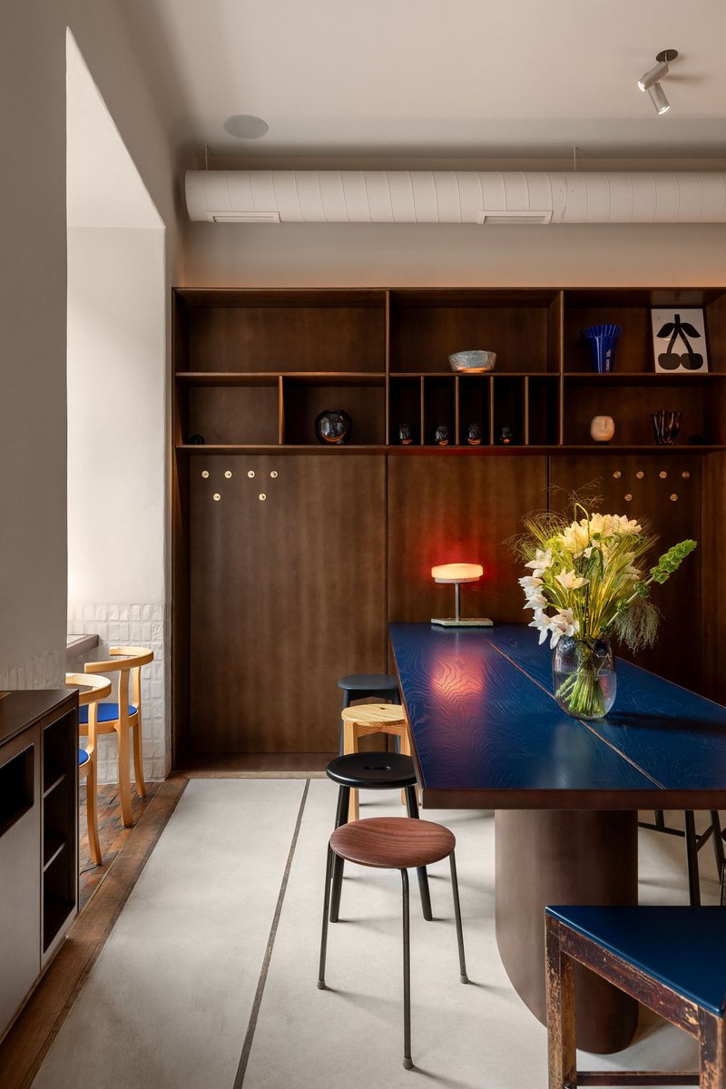 Dining area with deep blue lacquered table and walnut millwork wall beneath white ribbed ceiling panels