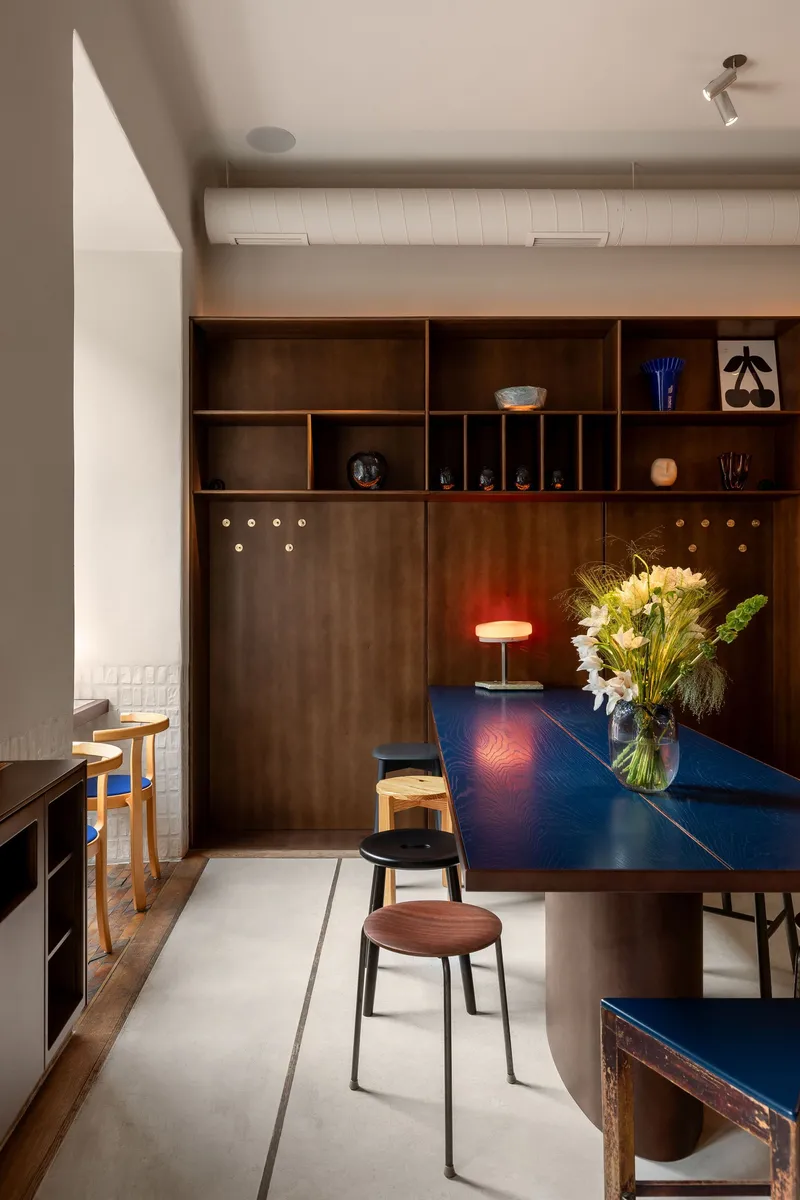Dining area with deep blue lacquered table and walnut millwork wall beneath white ribbed ceiling panels