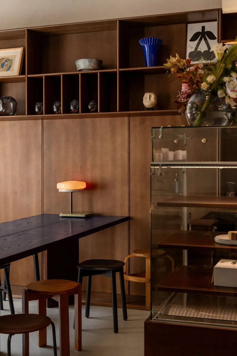 Walnut shelving unit with brass door pulls beside a glass-fronted vitrine displaying ceramics and glassware