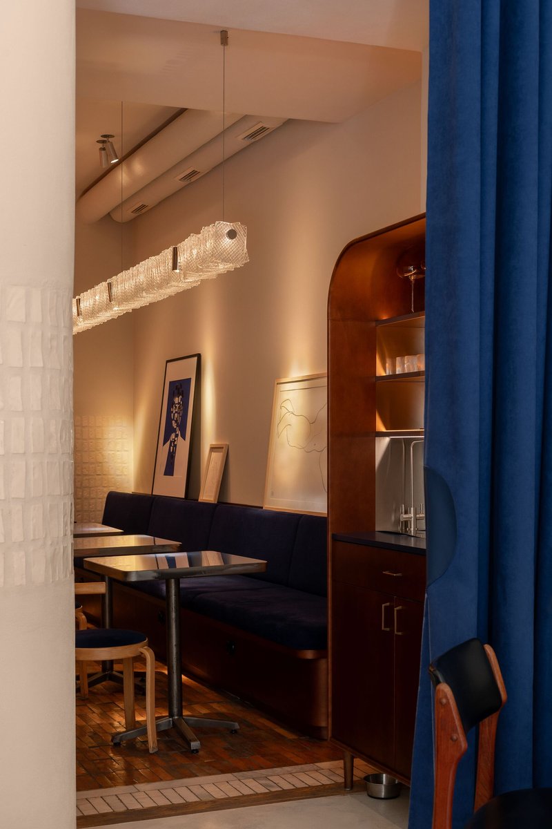 Banquette seating beneath a textured glass pendant light with blue fabric curtain at the entry