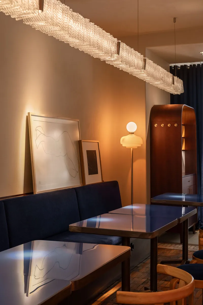 Banquette with leaning artwork beneath a long ridged glass pendant casting warm light across parquet flooring