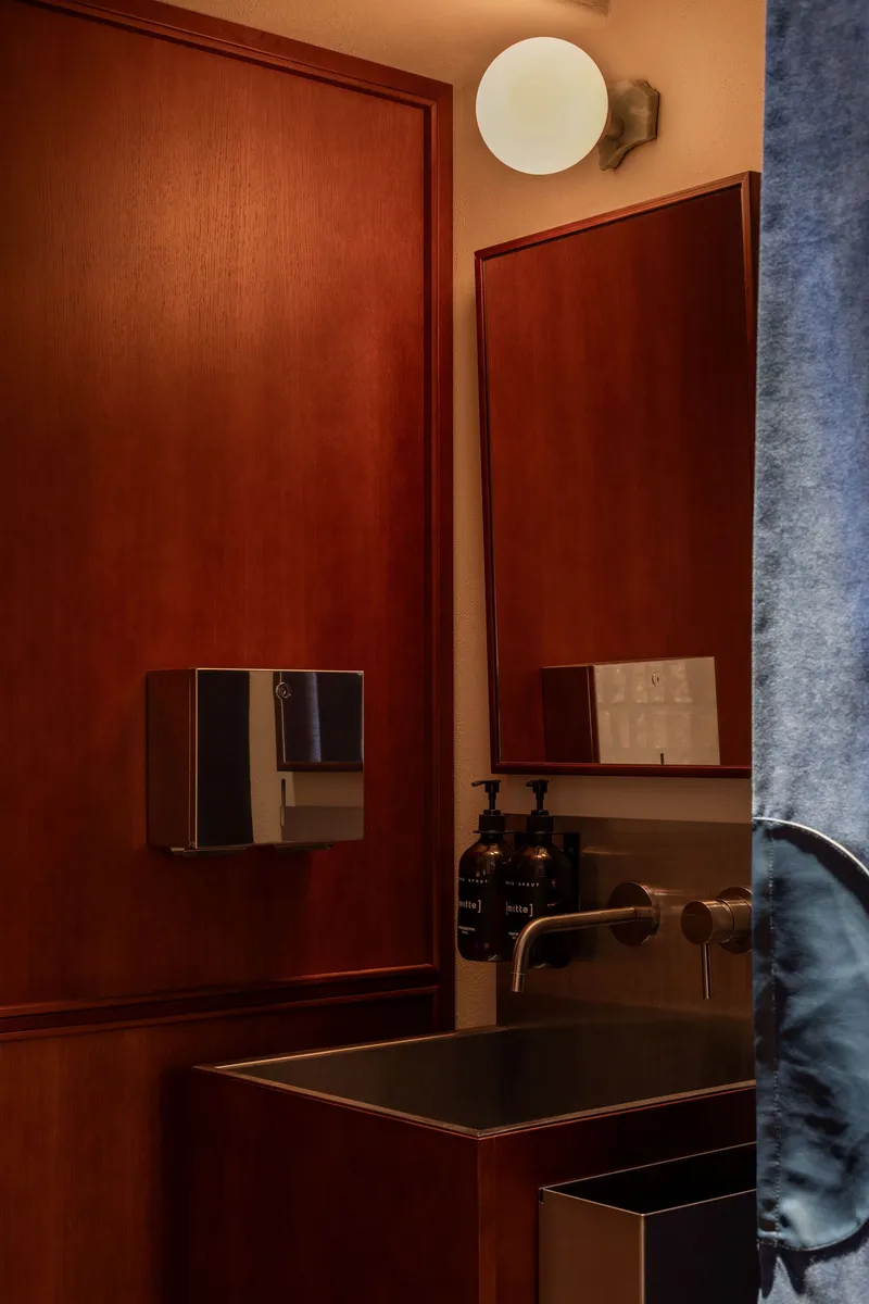 Bathroom vanity with wood paneling, brass faucet, black basin, and circular wall-mounted light fixture