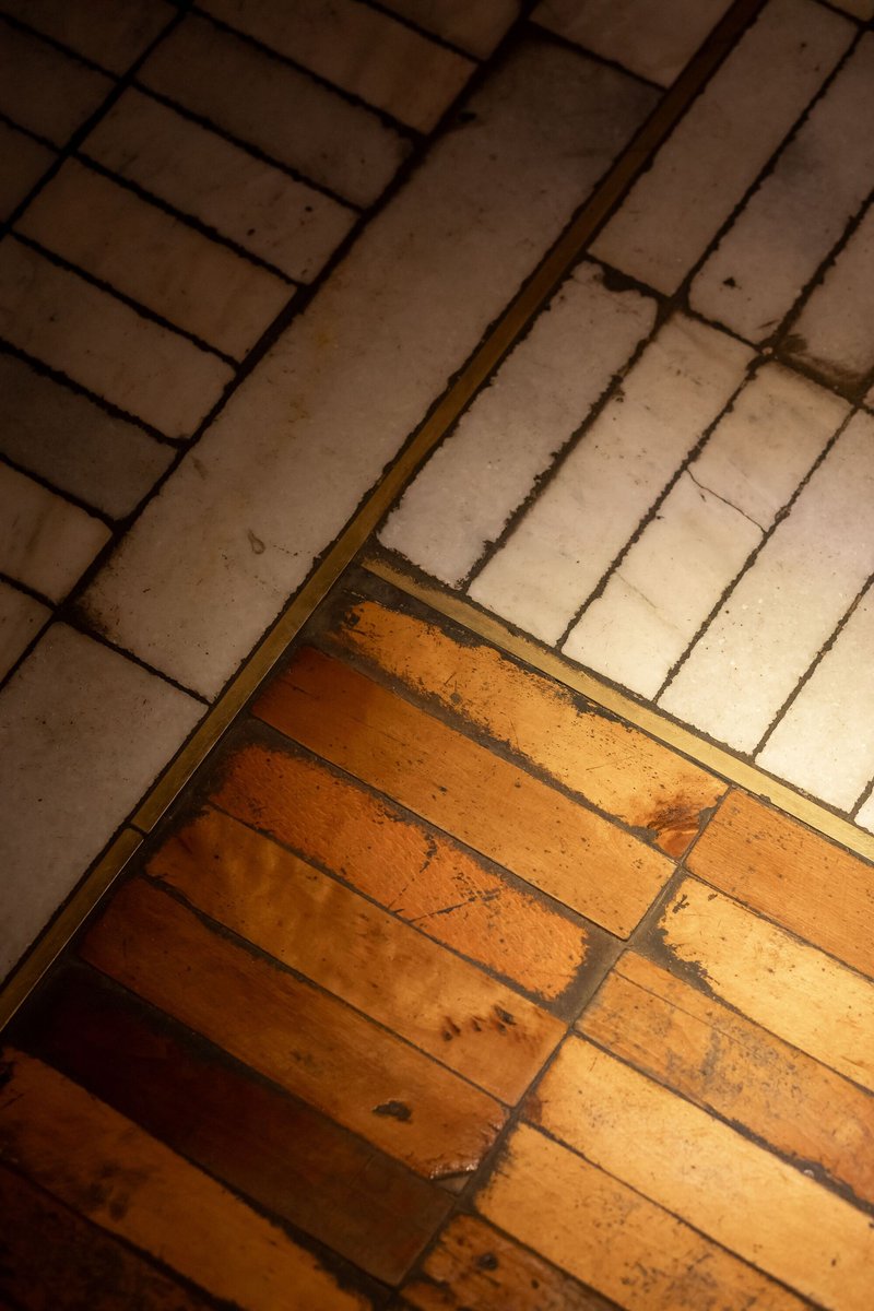 Diagonal threshold where weathered timber floorboards meet white ceramic tiles at differing orientations