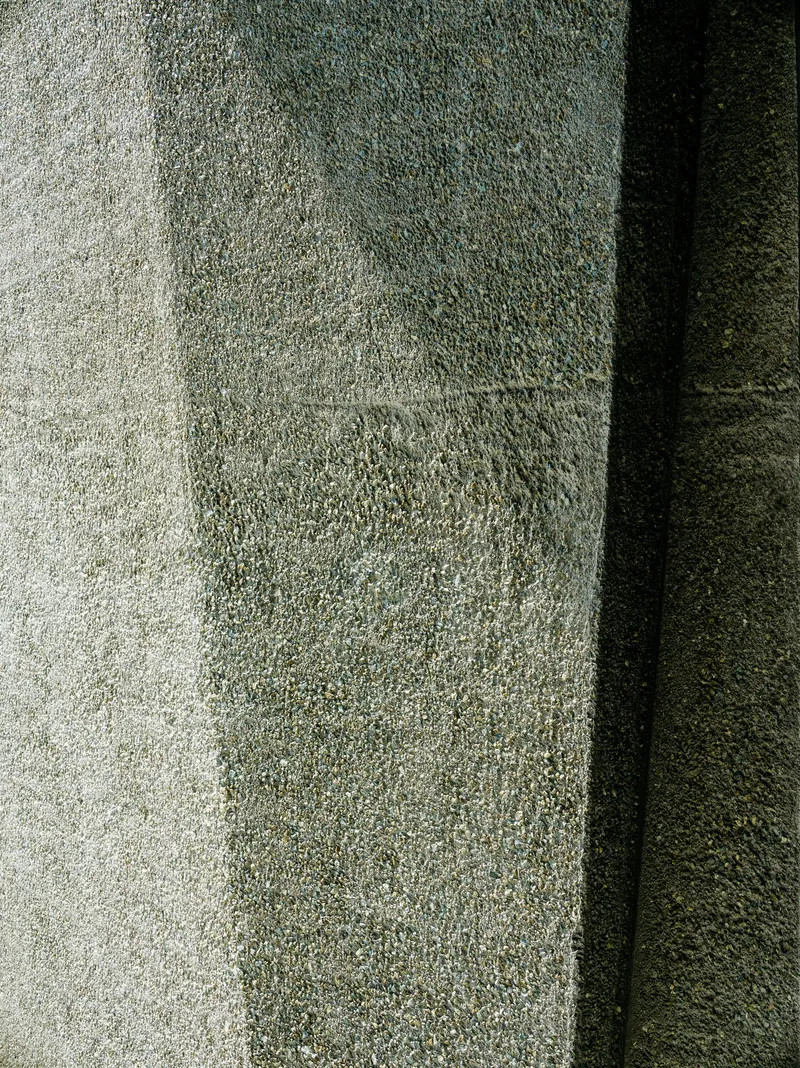 Close-up of textured concrete wall surface meeting a sharp vertical shadow line