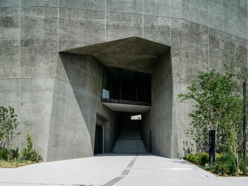 Angled concrete entrance portal framing an interior staircase with a suspended viewing box above