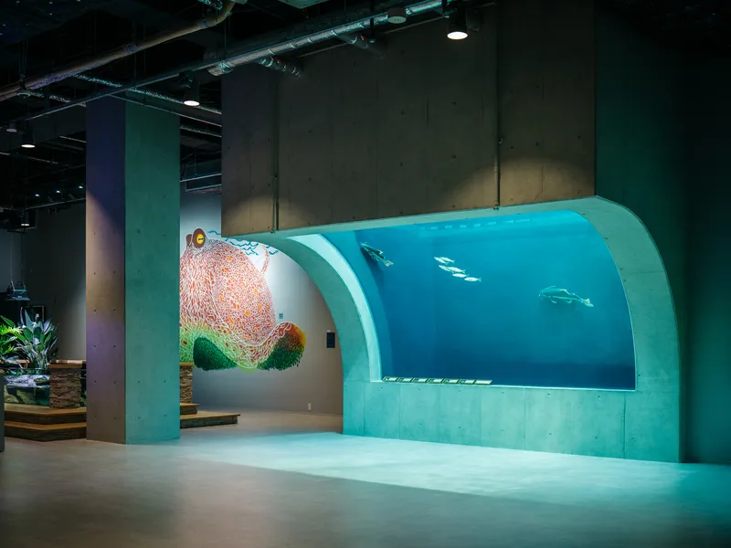 Curved aquarium viewing window with turquoise panels and penguins swimming in blue water