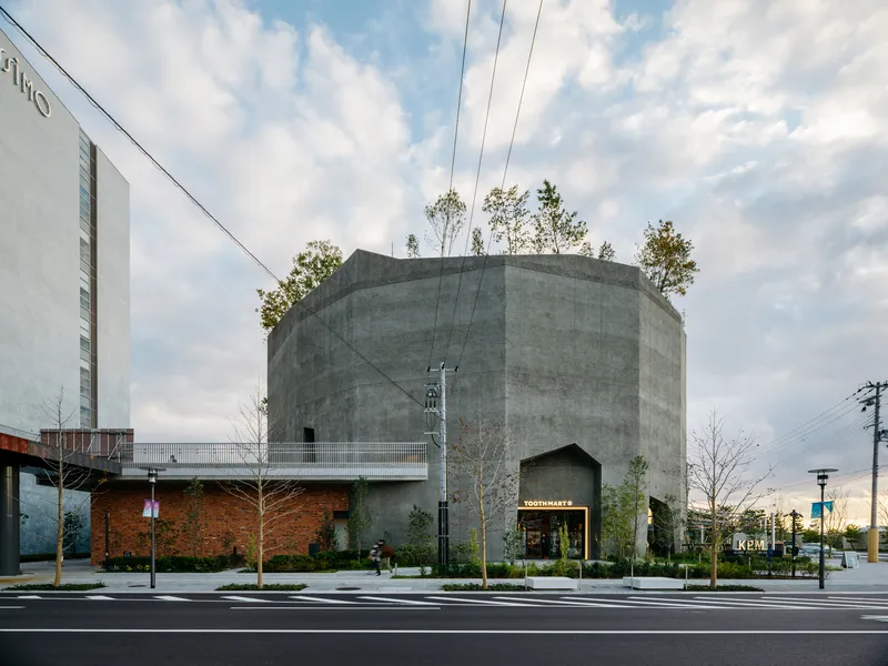 Street view of a cylindrical concrete tower with rooftop trees under a cloudy afternoon sky