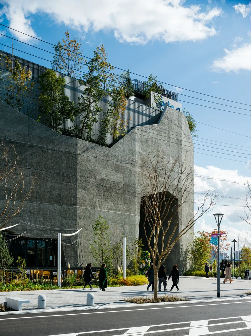 Concrete facade with planted terraces and pedestrians crossing the street in front on a sunny day