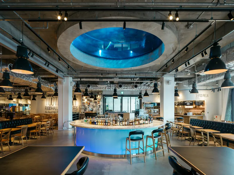 Restaurant interior with central bar beneath a circular aquarium opening in the ceiling