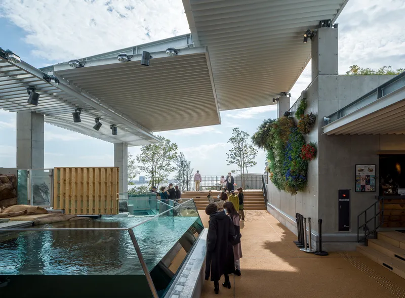 Rooftop terrace with shallow pool and visitors beneath cantilevered metal canopies on a cloudy day