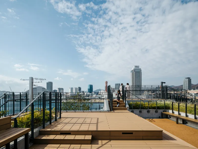 Rooftop terrace with timber decking and black metal railings overlooking the waterfront skyline under scattered clouds
