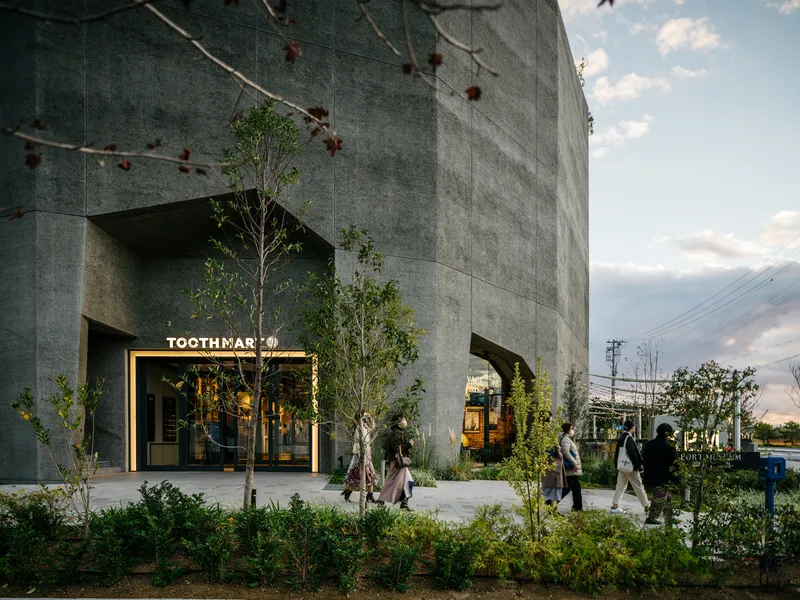 Concrete facade with arched openings and planted garden where pedestrians gather at golden hour