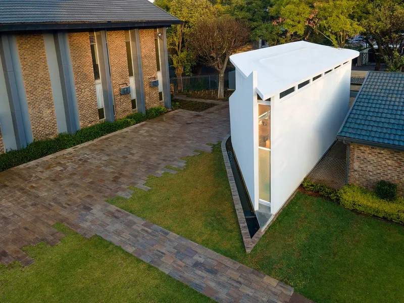 Drone perspective showing the cantilevered white form with horizontal slot windows opening toward the lawn