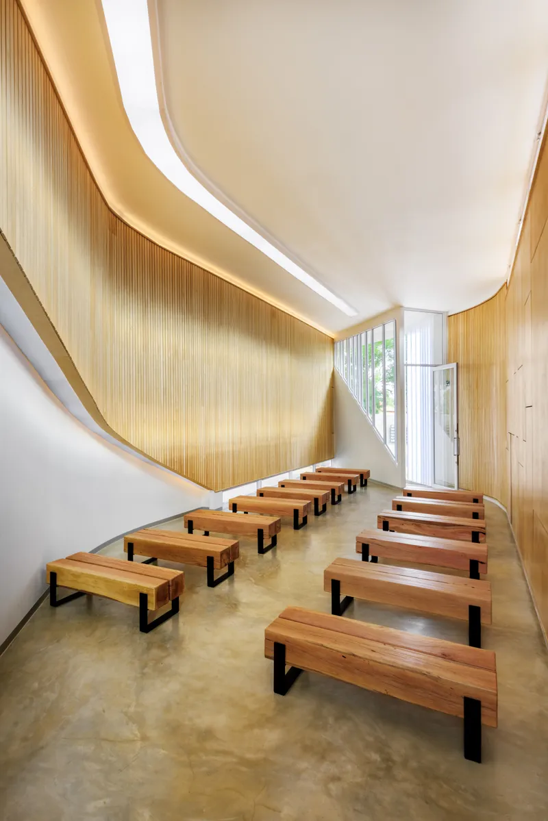 Interior chapel space with timber bench seating and curved timber slat walls lit by concealed cove lighting
