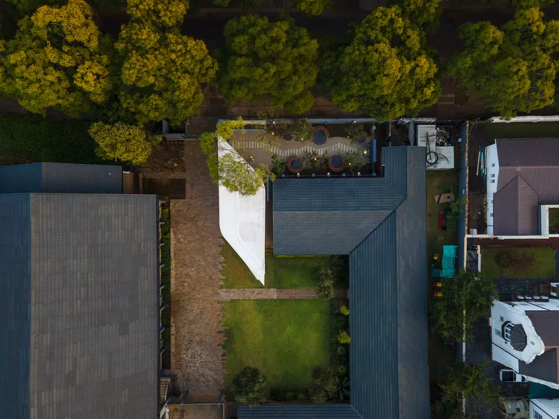 Top-down view of the white chapel volume nestled between residential properties with tiled roofs and garden plots