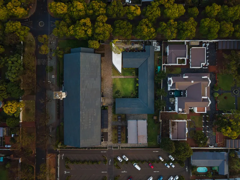 Aerial view of the rectangular building with dark tiled roofs surrounded by autumn trees and street parking