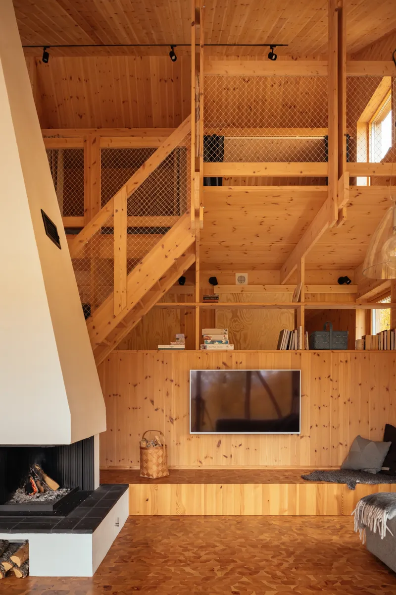 Double-height living space with layered timber platforms, mesh safety barriers, and integrated storage shelving
