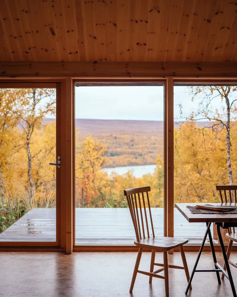 Timber-framed glass door opening to a deck overlooking a lake valley in autumn light
