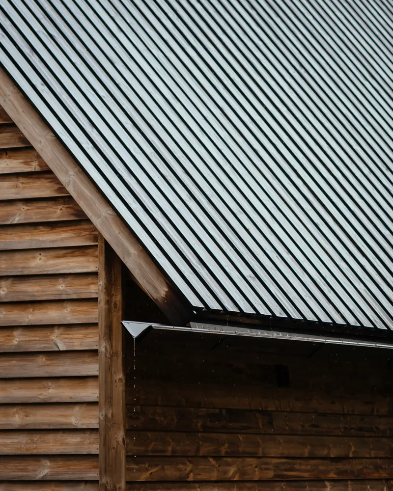 Junction of corrugated metal roofing and horizontal timber siding with exposed gutter