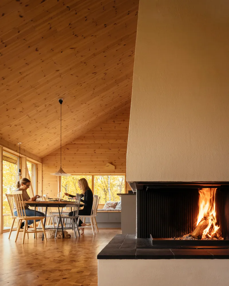 Two people seated at the dining table beside a black metal fireplace with active flames
