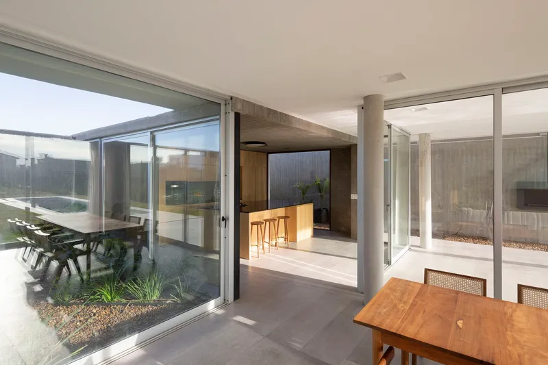 Glass-enclosed courtyard with planted bed adjoining an interior kitchen and timber dining table