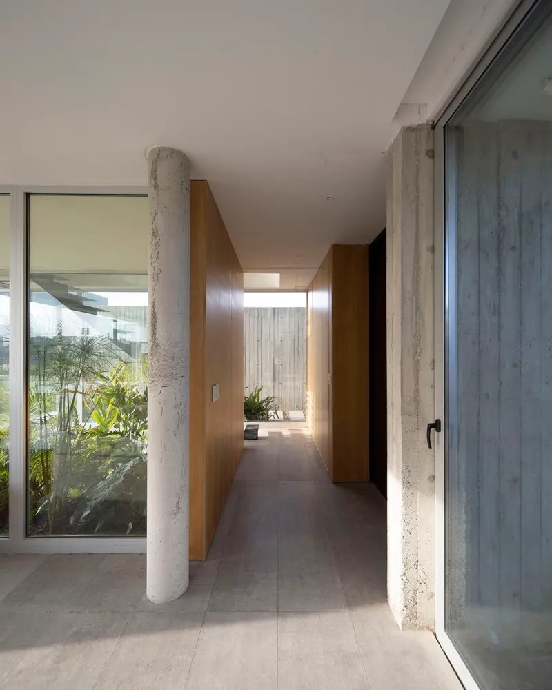 Interior corridor with exposed concrete columns flanked by glazing opening to planted courtyards