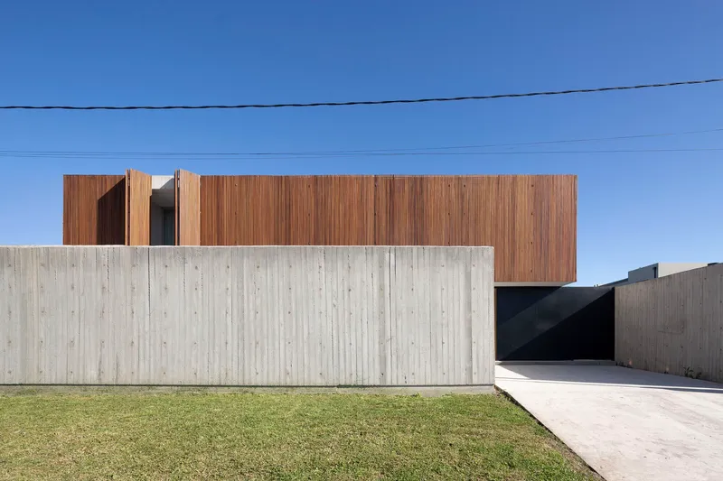 Street view of the layered facade with vertical timber cladding above a board-formed concrete base and lawn