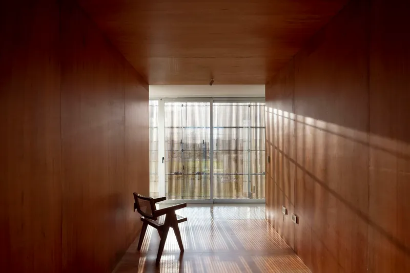 Wood-paneled room with a single chair facing a translucent glazed wall filtering diagonal sunlight